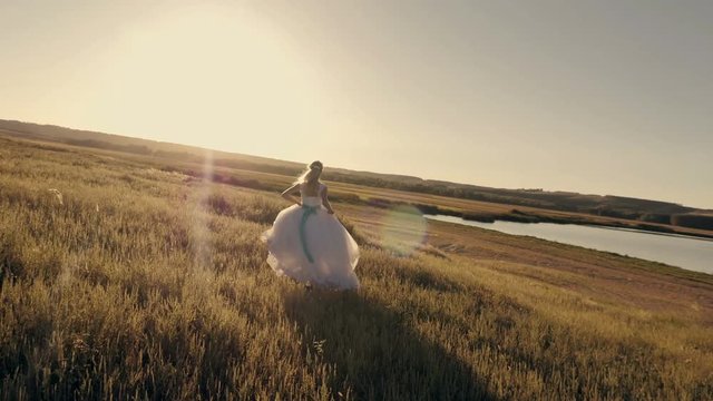 Bride running across the field to meet the sun at sunset, slow motion
