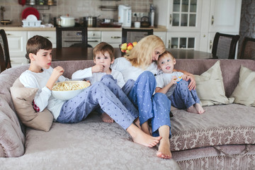 mother and sons are sitting on the couch watching television with popcorn in the kitchen