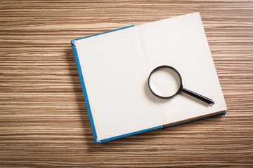 Magnifying glass and book o the wooden background