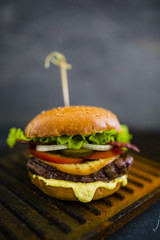 Tasty grilled beef burger in crispy shortbread with lettuce and fresh vegetables on stone dark background. Street food with space for text.