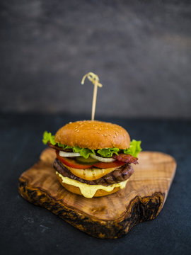 Tasty street food grilled beef burger in crispy shortbread with lettuce and fresh vegetables on stone dark background. Fast food with space for text.