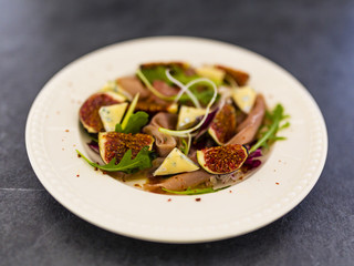 Figs and gorgonzola and prosciutto with arugula leaves served on a plate.