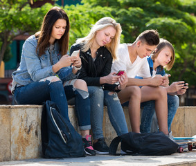 Teenagers sitting and looking at their mobile phones