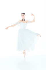 Ballerina in white dress posing on pointe shoes, studio background.