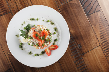 Olivier salad with trout in a white plate. Wooden background