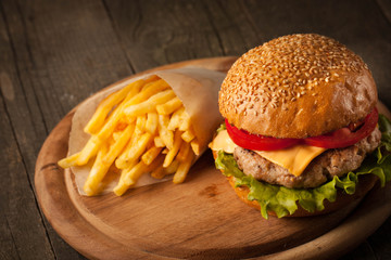 Home made hamburger with beef, onion, tomato, lettuce and cheese. Fresh burger closeup on wooden rustic table with potato fries, beer and chips.