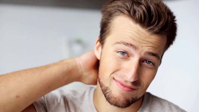 face of happy smiling young man touching hair