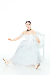 Ballerina in white dress sitting, studio background.