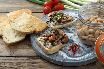 crostini di pane e fagioli bianchi con pomodoro su sfondo tavolo di cucina rustico