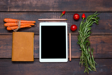 The tablet, notebook, fresh bitter and sweet pepper on wooden table background