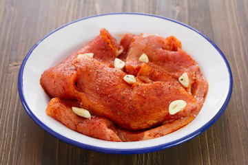marinated meat with garlic on white dish on brown wooden background