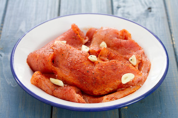 marinated meat with garlic on white dish on blue wooden background