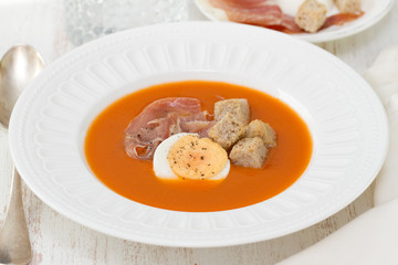 tomato cold soup with egg and jamon on white dish on whooden background