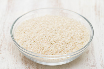 raw rice in bowl on white wooden background