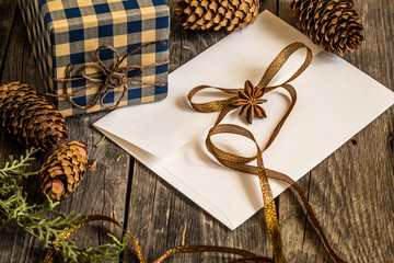 White envelope on wooden background with pine cones and Christmas gift