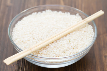 raw rice in bowl on brown wooden background
