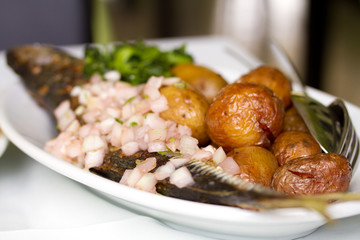 fish with potato and greens on white plate on table