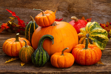 pile of orange and green pumpkins with fall leaves on wooden table