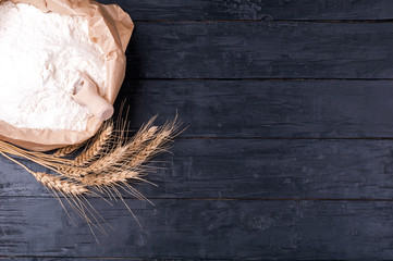 Baking background. Flour in paper bag and wheat on dark wooden table. Ingredients for cooking.  Top view