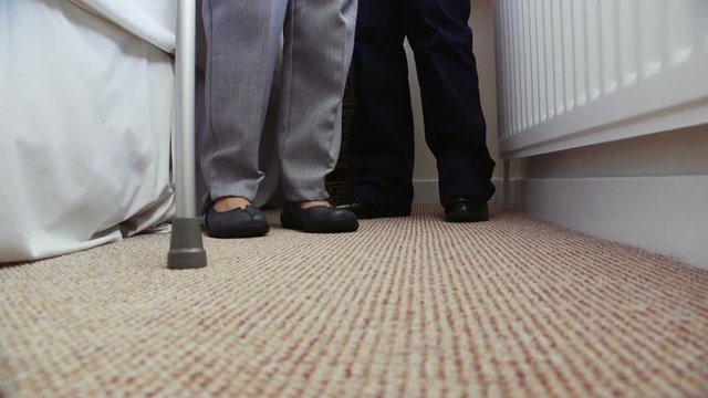 Close up of a senior womans legs as she gets off the bed with the assistance of a home caregiver and a walking stick.