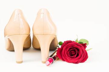 Nude colored high heels still life with red rose bud and lipstick