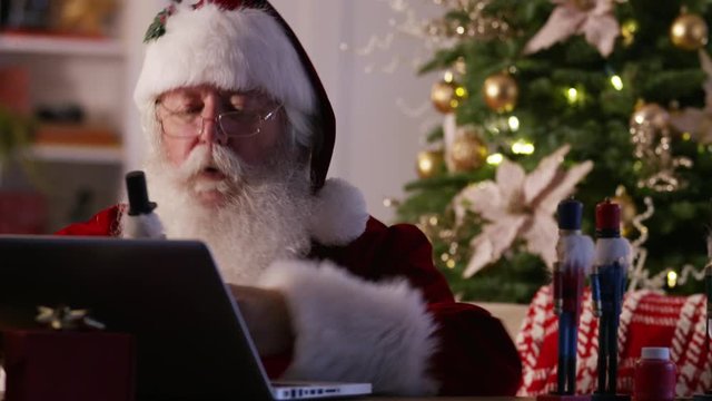 Santa Claus in workshop using laptop computer