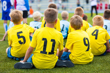 Children soccer football team at the sport stadium. Boys sitting on football pitch during school...