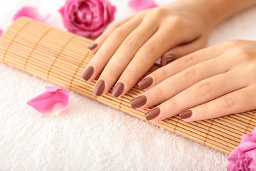 Female hands with brown manicure on wicker bamboo mat