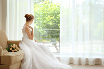Fototapeta premium Bride in beautiful dress with wedding bouquet sitting on sofa