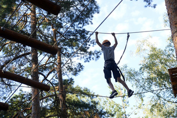 Portrait of active brave boy enjoying outbound climbing at adventure park on tree top