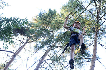 Portrait of active brave boy enjoying outbound climbing at adventure park on tree top