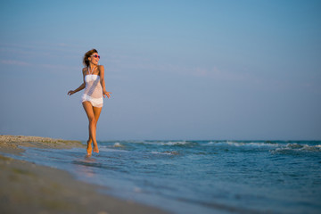 Fototapeta na wymiar Happy girl in white bathing suit. girl walking along the beach. Caucasian woman walks along beautiful seashore 