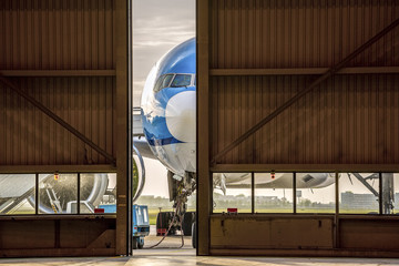 Airplane in front of half opened door to hangar - obrazy, fototapety, plakaty