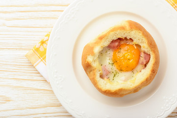 Bun baked with egg, cheese  and ham on white wooden table.