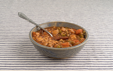 Bowl of beef stew with spoon on a striped tablecloth with a spoon inserted into the food.