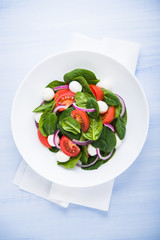 Fresh salad with mozzarella cheese, tomato, spinach and purple onion on blue wooden background top view. Healthy food.