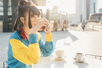 young beautiful asian millennial woman nonconformist sitting outdoor in a bar in city back light...