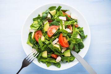 Fresh healthy salad with chicken, tomatoes, spinach and avocado on blue wooden background top view. Health and food.