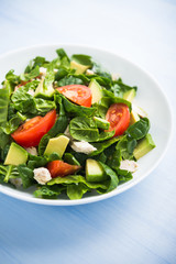 Fresh healthy salad with chicken, tomatoes, spinach and avocado on blue wooden background close up. Health and food.