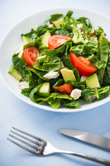 Fresh healthy salad with chicken, tomatoes, spinach and avocado on blue wooden background close up. Health and food.