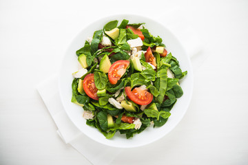 Fresh salad with chicken, tomatoes, spinach and avocado on white wooden background top view....