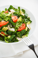 Fresh salad with chicken, tomatoes, spinach and avocado on white wooden background close up. Healthy food.