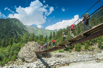 Group of hikers goes above the mountain river - obrazy, fototapety, plakaty