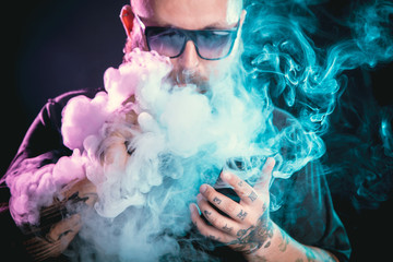 Men with beard  in sunglasses vaping and releases a cloud of vapor.
