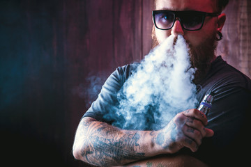 Men with beard  in sunglasses vaping and releases a cloud of vapor.