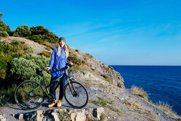 Fototapeta premium attractive young smiling blonde woman with the bike standing on a rock