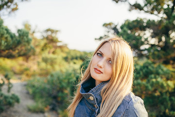 portrait of a beautiful young blonde woman in denim jacket standing with folded hands outdoor
