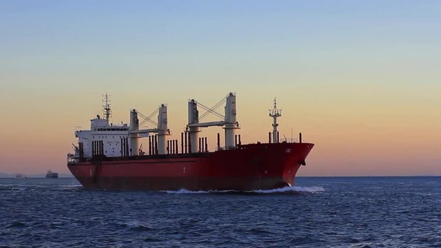 Cargo ship sailing from open sea. A bulk carrier ship with deck cranes on the sunset time. 