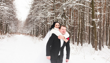 Man giving woman piggyback ride on winter vacation in snowy forest.