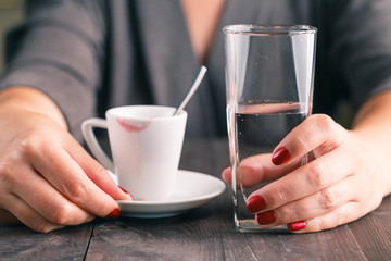Cup of coffee on a wooden table with glass of water in woman han